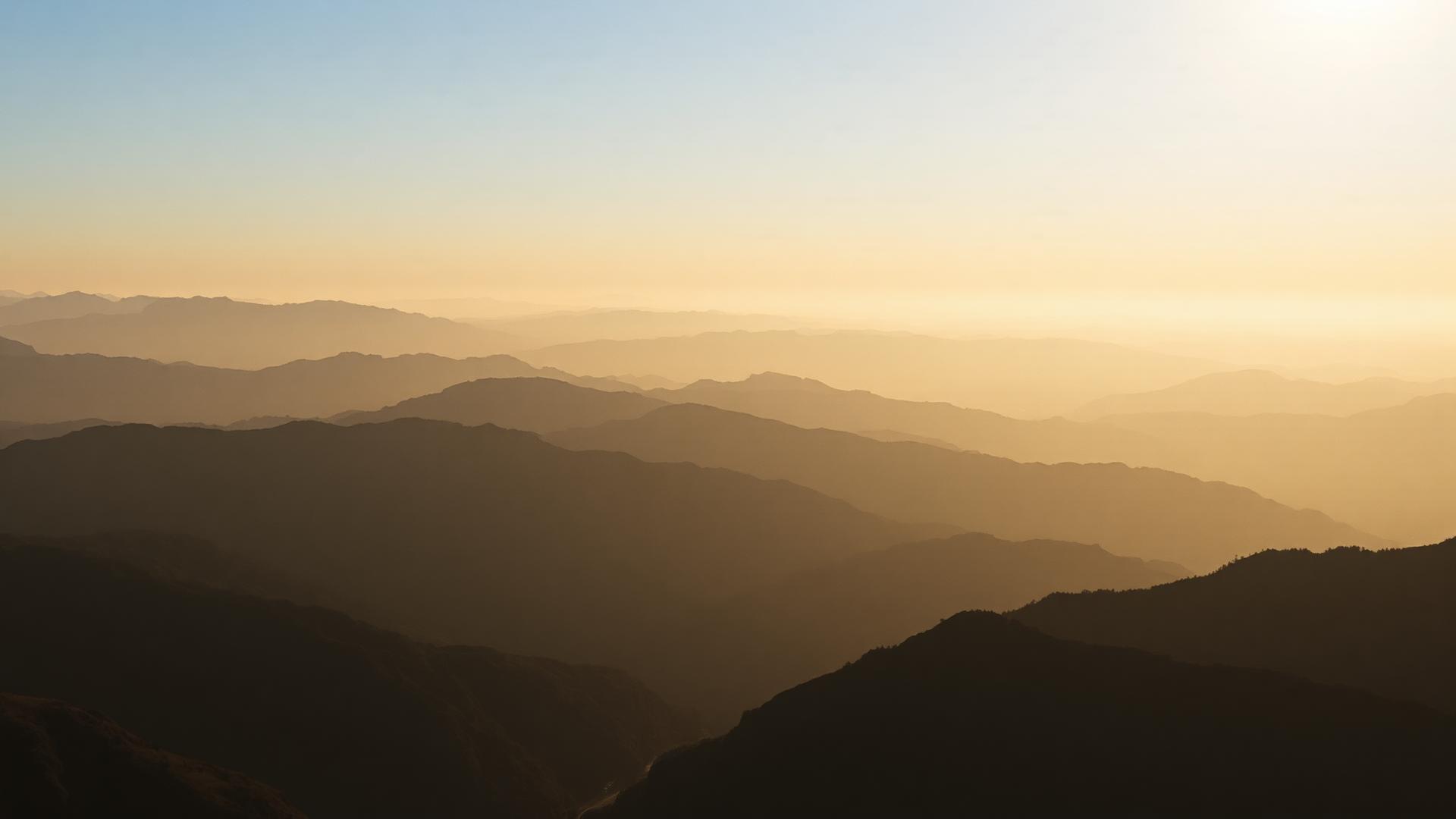 Layered mountain ranges fading into golden morning haze.